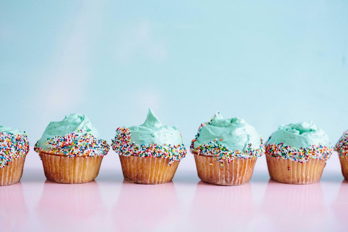 A row of vanilla cupcakes with mint-green frosting and rainbow sprinkles