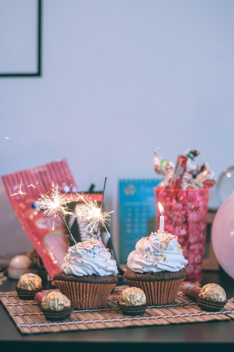 Due cupcake al cioccolato con glassa bianca e codette colorate, uno con una candelina di compleanno accesa