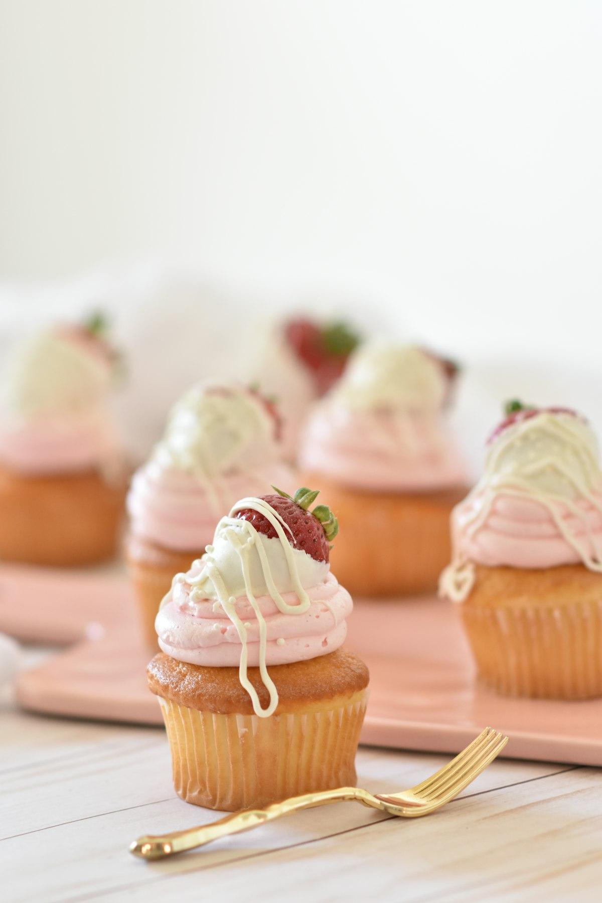 Un cupcake alla fragola con frosting rosa, un filo di cioccolato bianco e una fragola fresca