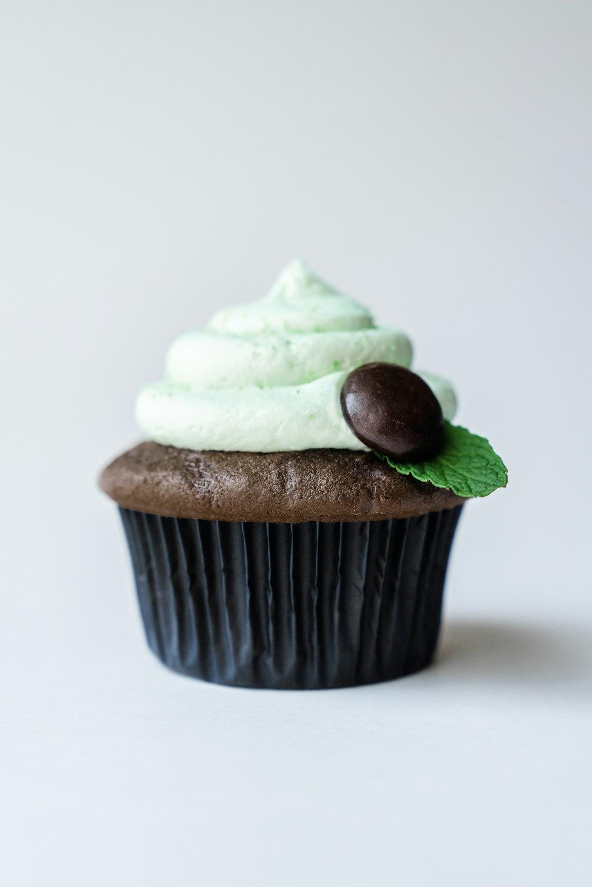 Un cupcake al cioccolato con frosting verde menta pallido, un cioccolatino alla menta e una foglia di menta
