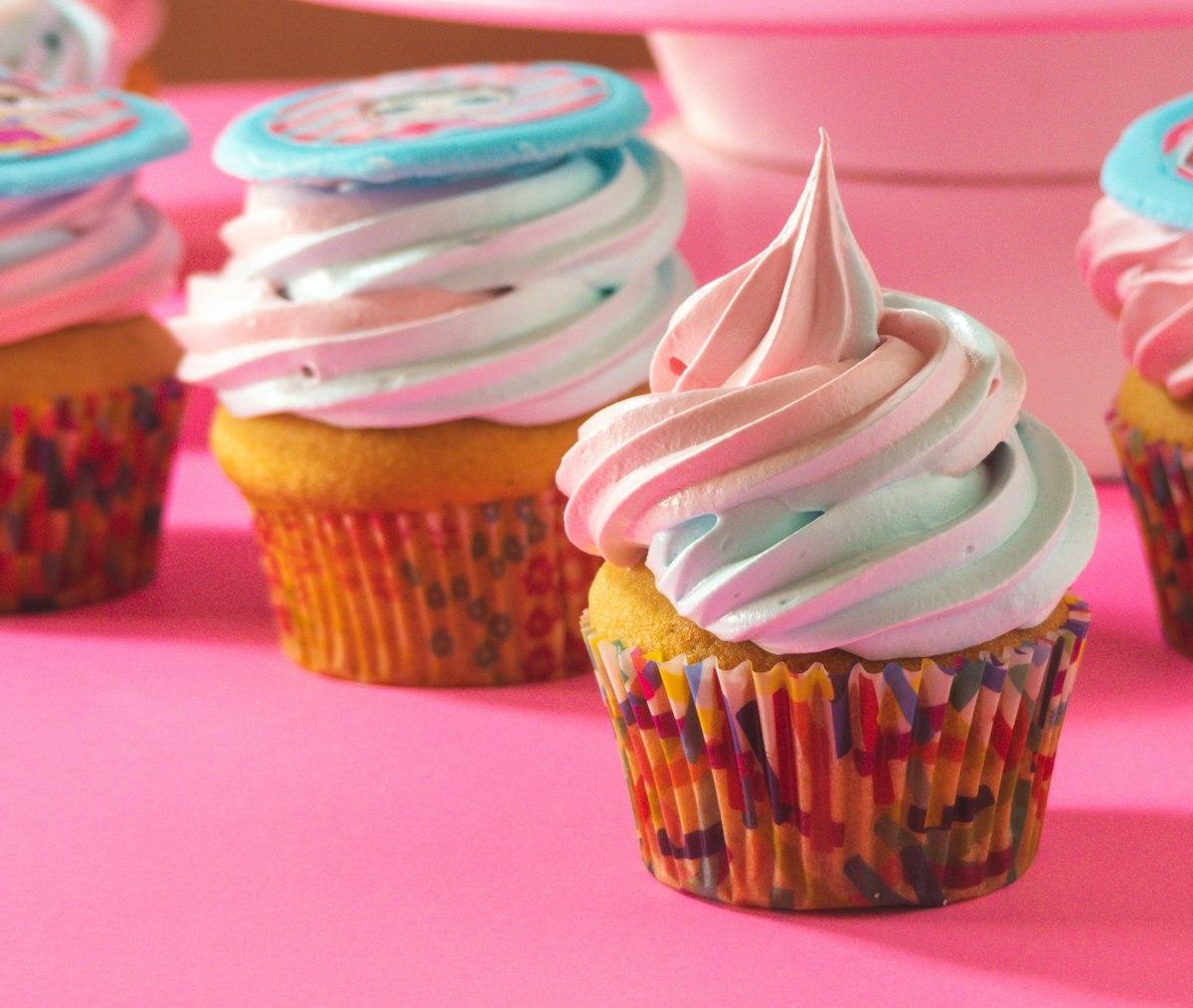 An assortment of cupcakes with pink and blue swirled buttercream in confetti liners